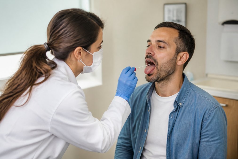 Un profesional de la salud con guantes y bata blanca tomando una muestra con un hisopo en un consultorio médico limpio y privado, mientras el paciente está sentado y tranquilo